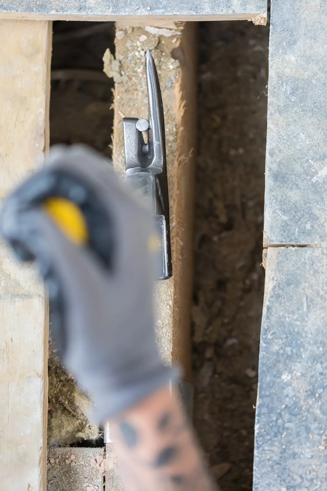 STANLEY STHT0-51312 Klauenhammer auf Holzbalken, Nahaufnahme mit unscharfer behandschuhter Hand vorn.