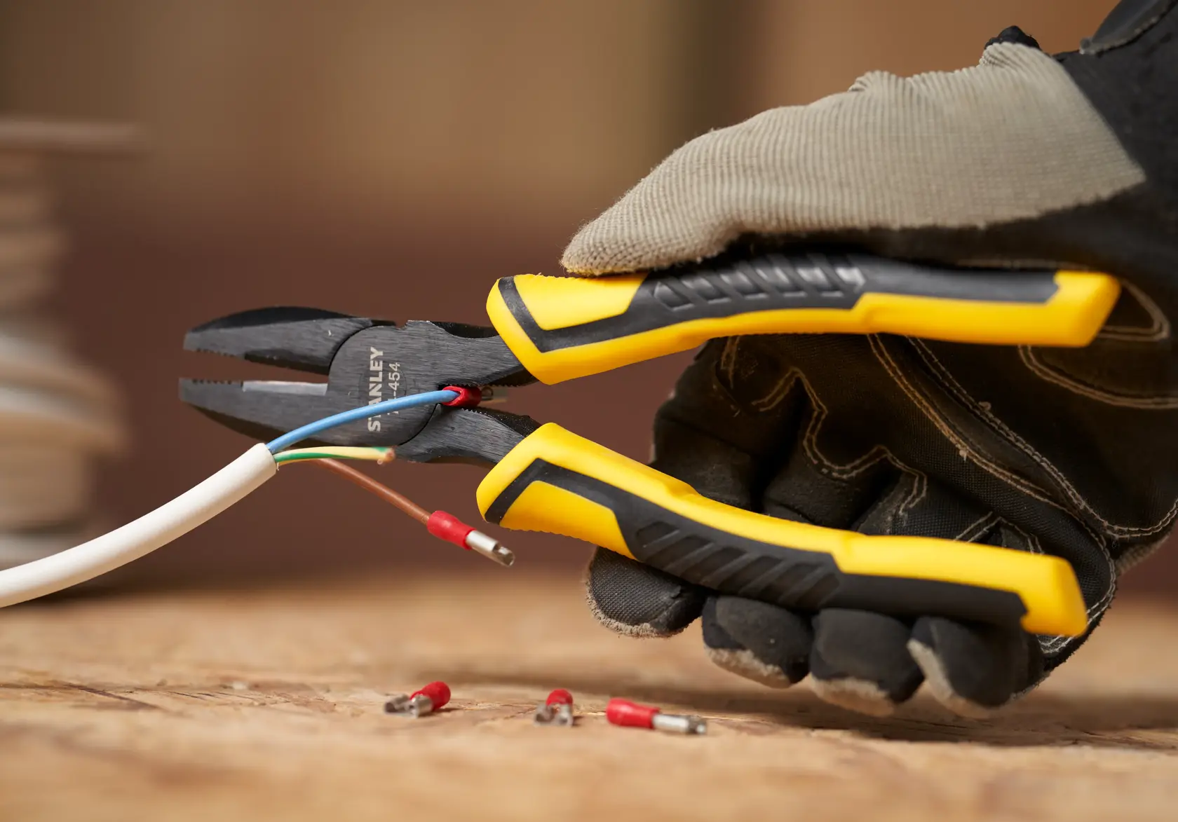 Foto der STANLEY STHT0-74454 Kombizange mit gelb-schwarzem Griff schneidet Elektrokabel, gehalten von behandschuhter Hand.