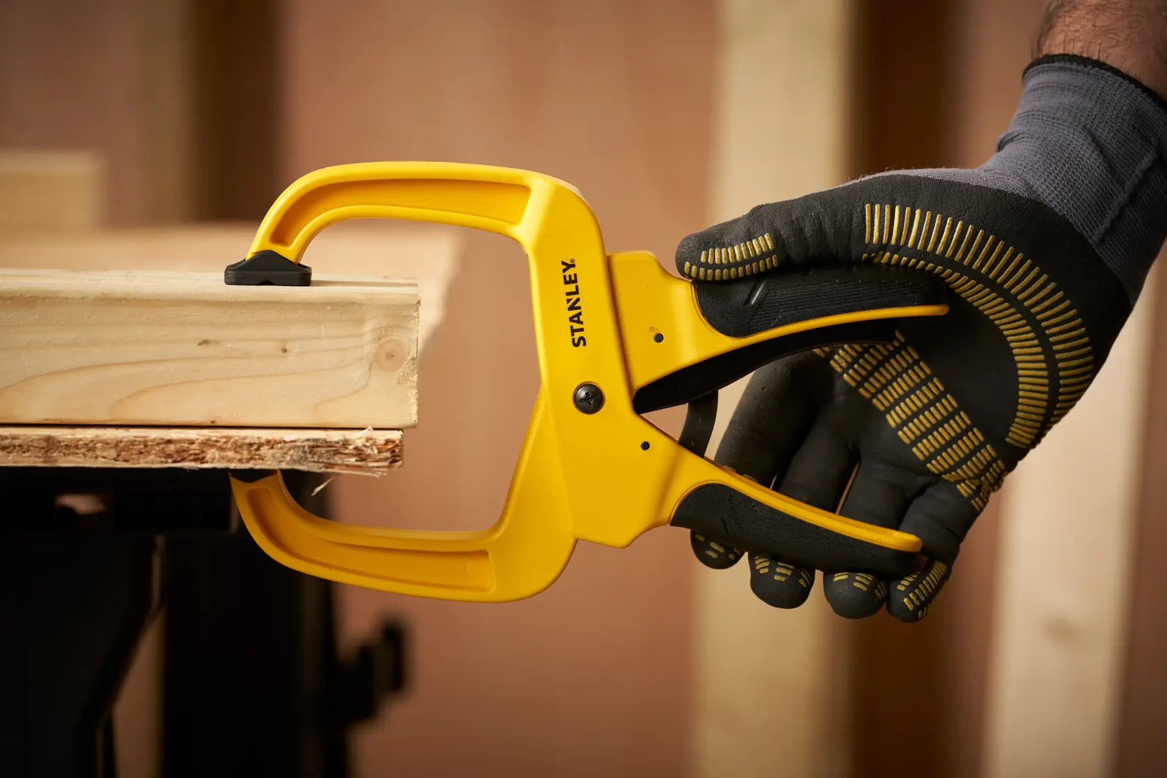 STANLEY STHT0-83200 Zwinge hält Holzbretter, behandschuhte Hand im Werkstatteinsatz.