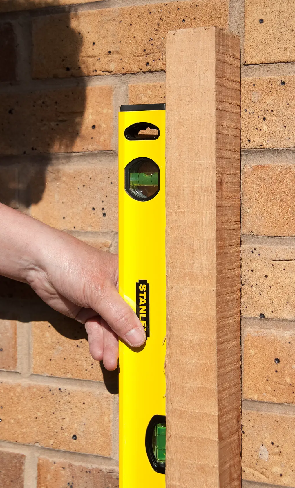 STANLEY STHT1-43103 gelbe Wasserwaage an Holz und Ziegelwand gehalten, Nahaufnahme.