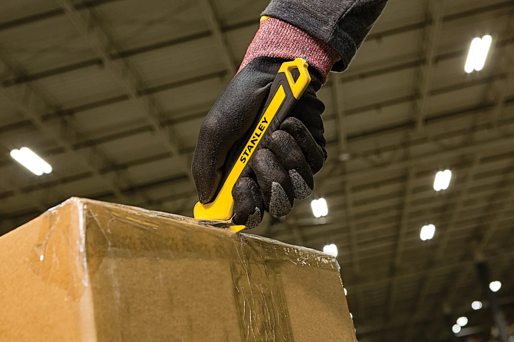 Foto von STANLEY STHT10356-0 Messer schneidet Karton, behandschuhte Hand im Lager.