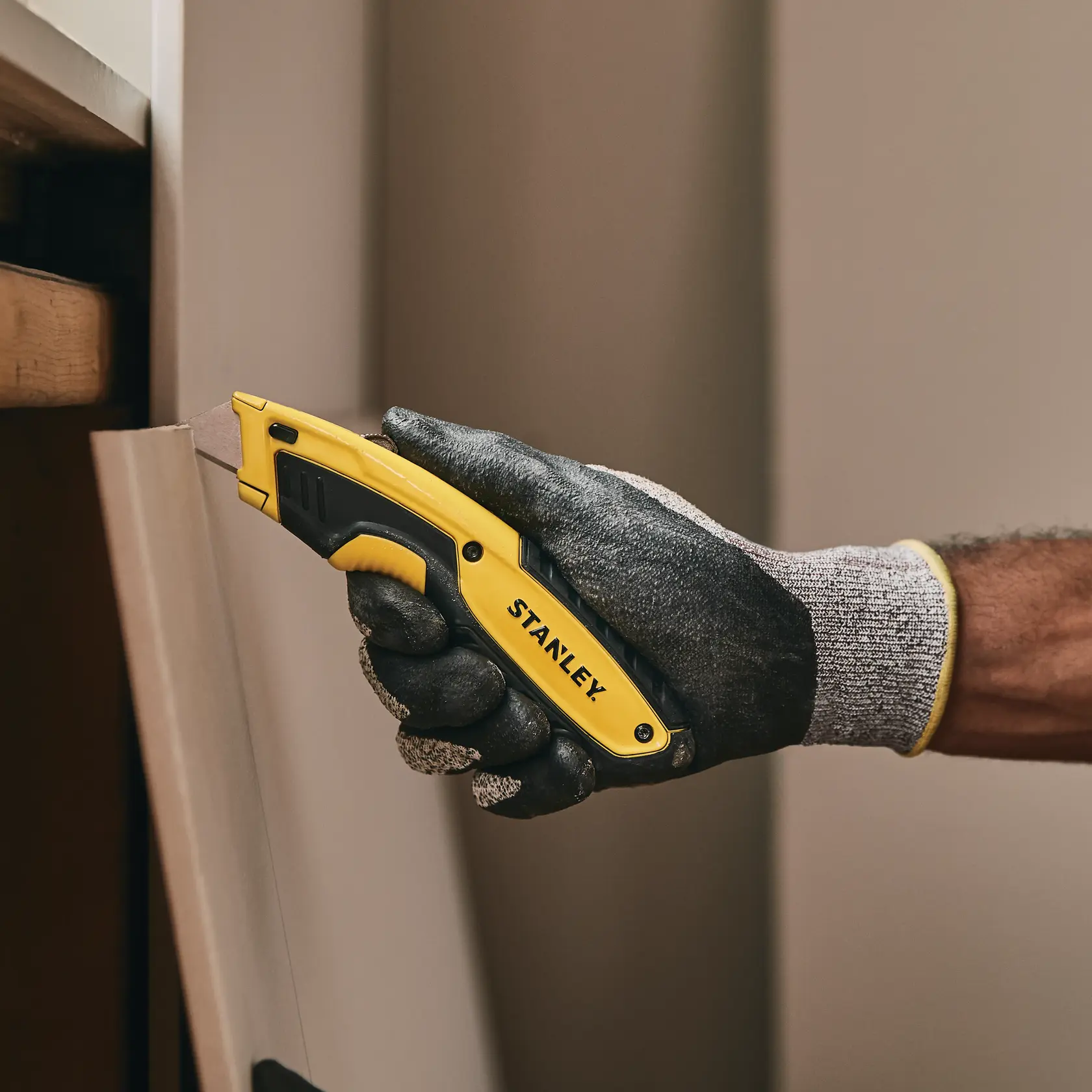 Foto vom STANLEY STHT10479-0 Universalmesser in behandschuhter Hand, schneidet eine Brettkante innen.