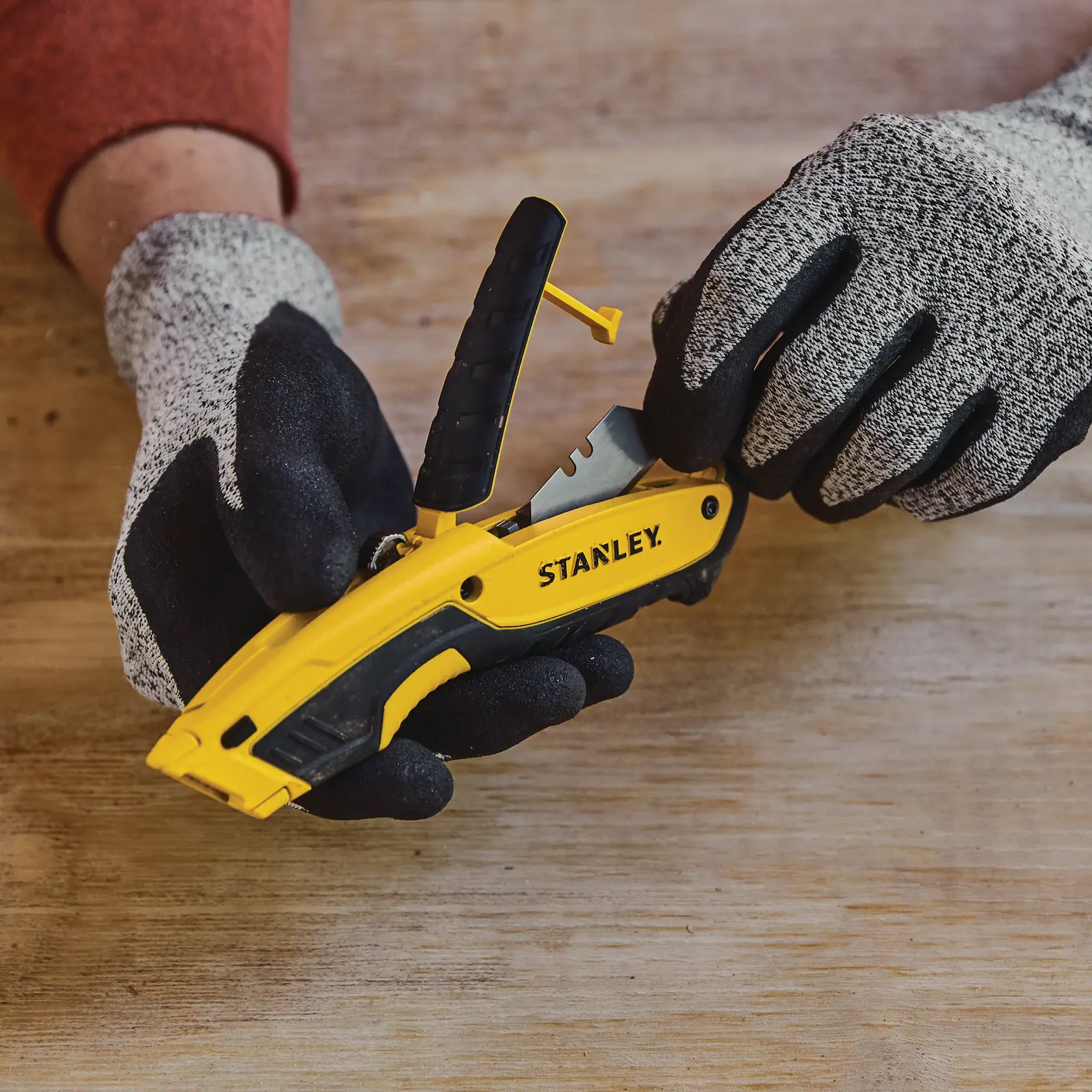 Foto des STANLEY STHT10479-0 Klappmessers mit Handschuhen, gelb-schwarz, auf Holztisch.