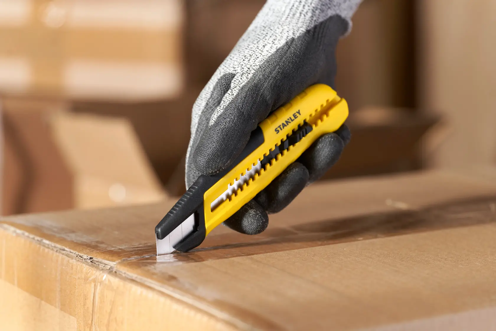 Foto von STANLEY STHT10489, STHT10489-0 gelbes Universalmesser, schneidet Karton, Handschuhhand, Fotografie.