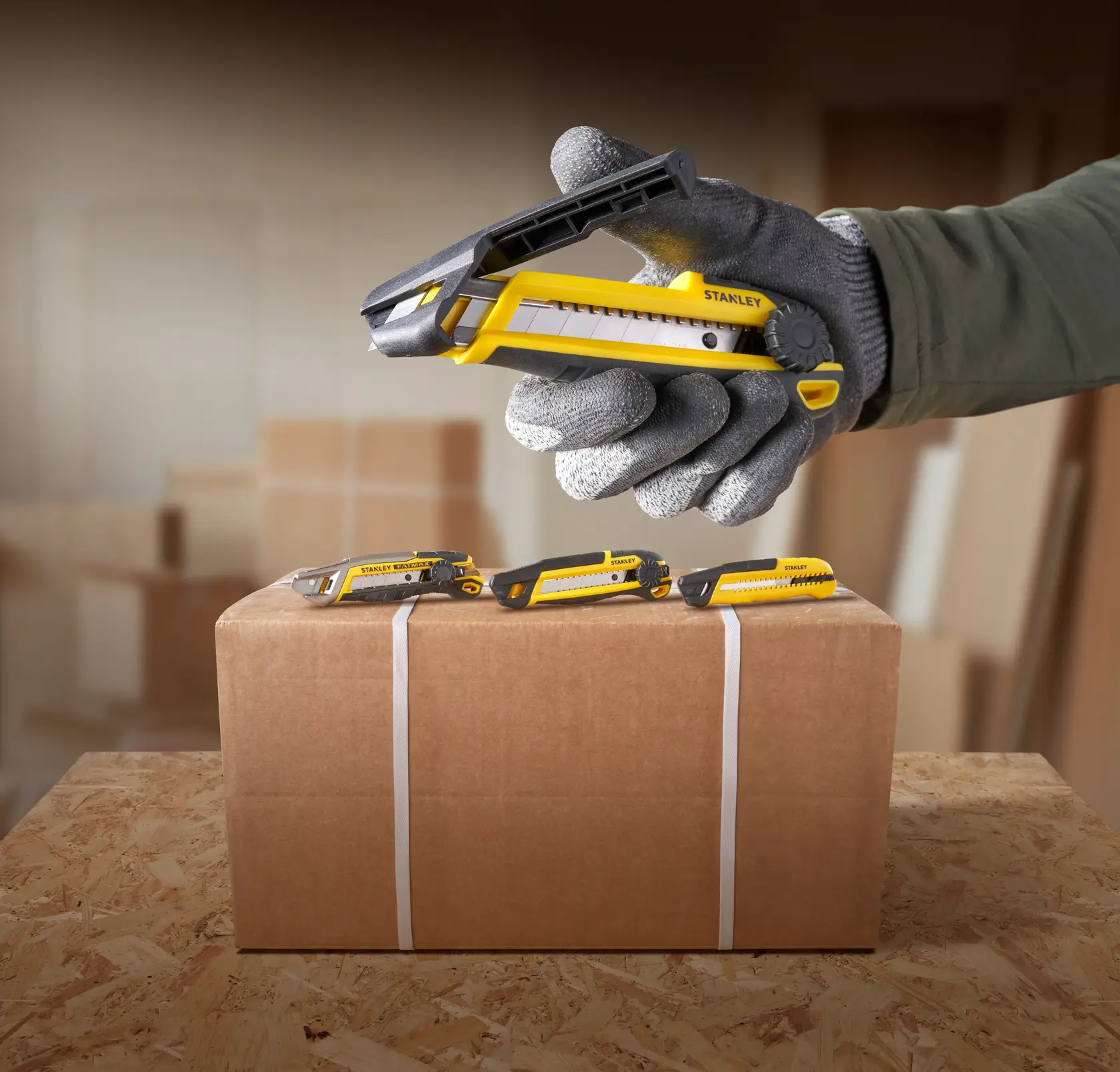 Foto des STANLEY STHT10500-0 Cuttermessers gelb-schwarz, schneidet Paketband, Hand mit Handschuh.