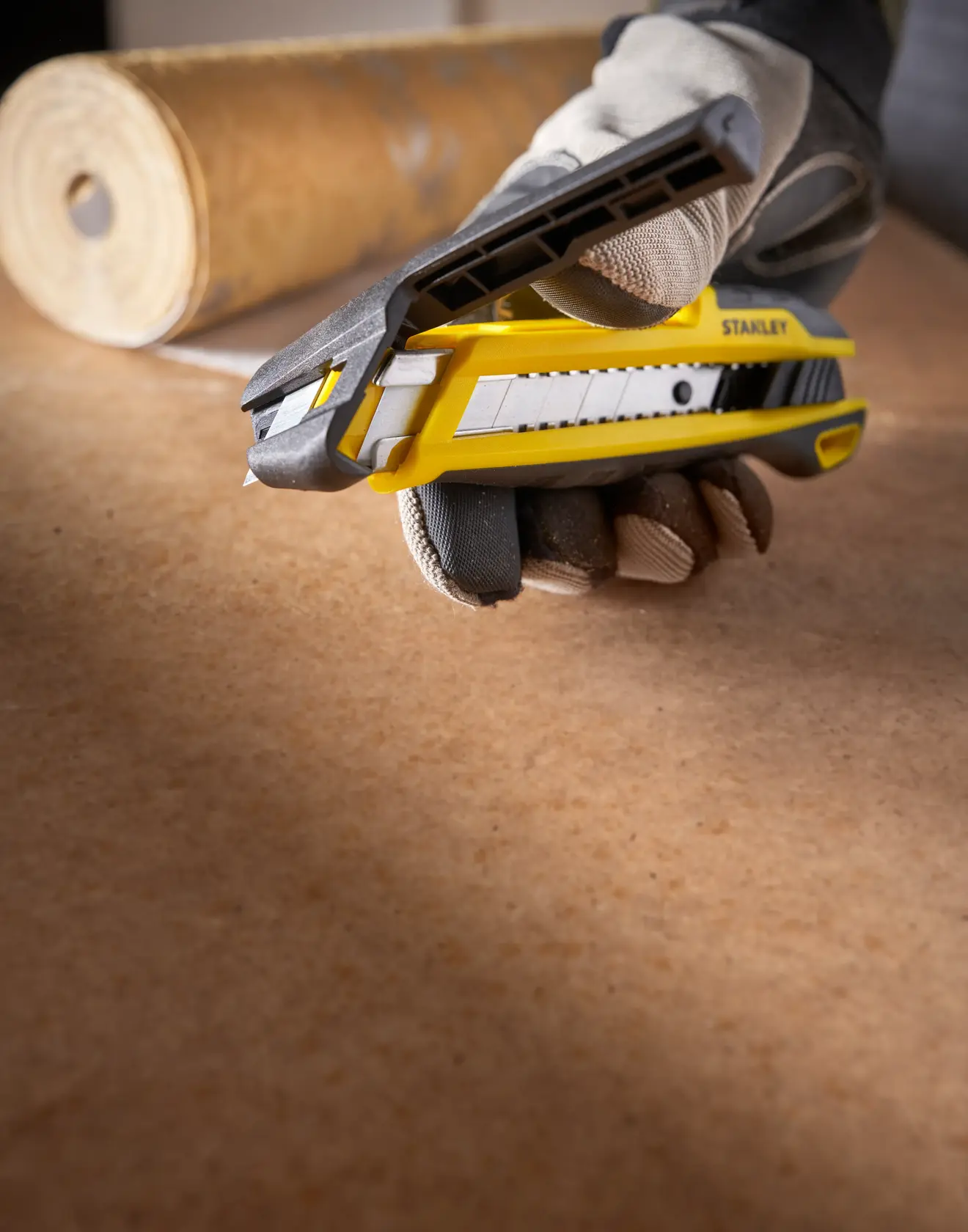 Foto von STANLEY STHT10501-0 Messer in behandschuhter Hand, Klinge ausgefahren auf Arbeitsfläche.