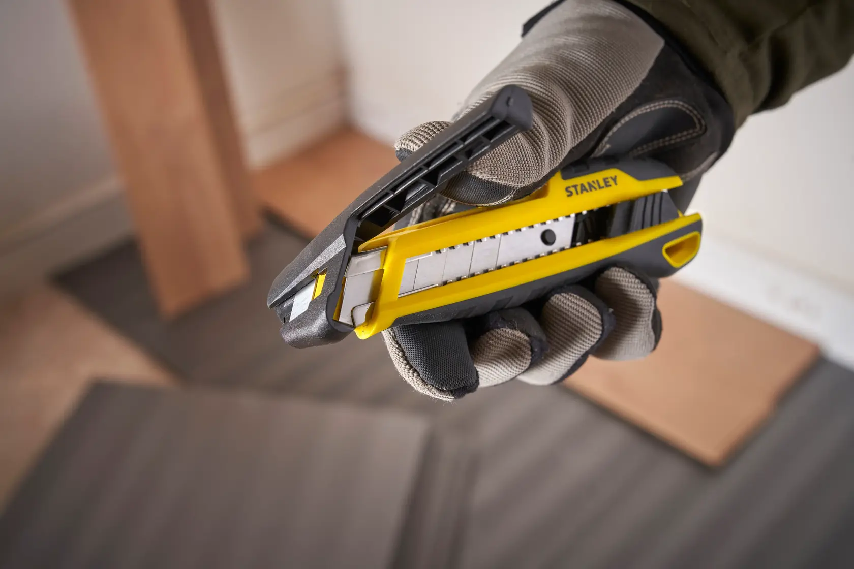 Foto des STANLEY STHT10501-0 Cuttermessers in behandschuhter Hand, gelb und schwarz, seitliche Ansicht.