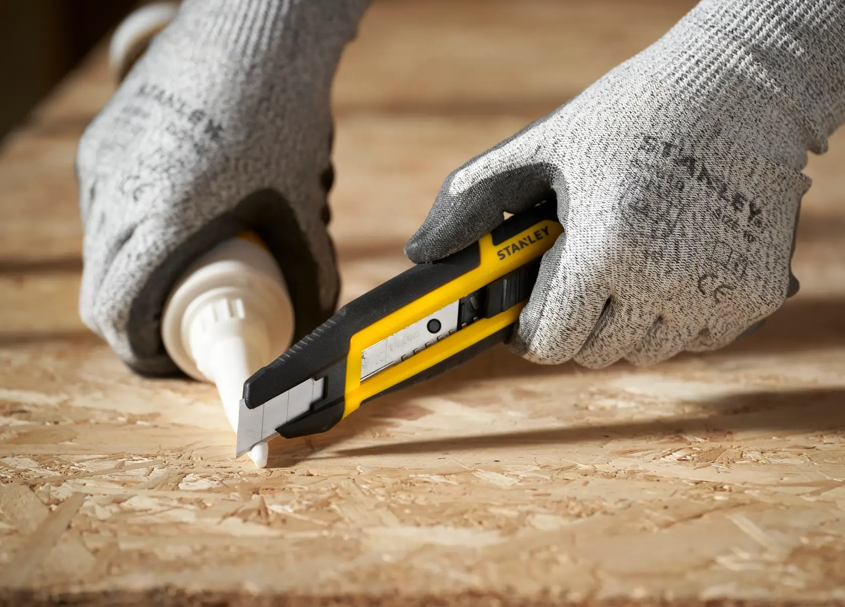 STANLEY STHT10501-0 Universalmesser in behandschuhter Hand, schneidet Holz auf Tisch, Seitenansicht.
