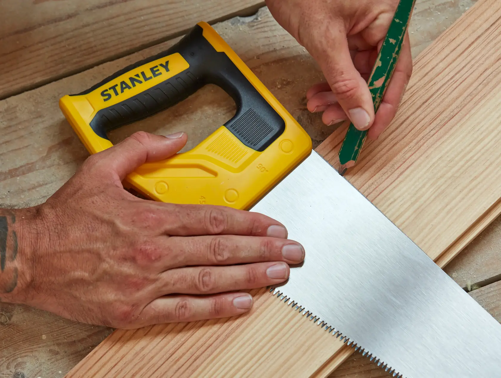 Stanley STHT20350-1 Handsäge mit gelb-schwarzem Griff auf Holz, Person markiert mit Bleistift.