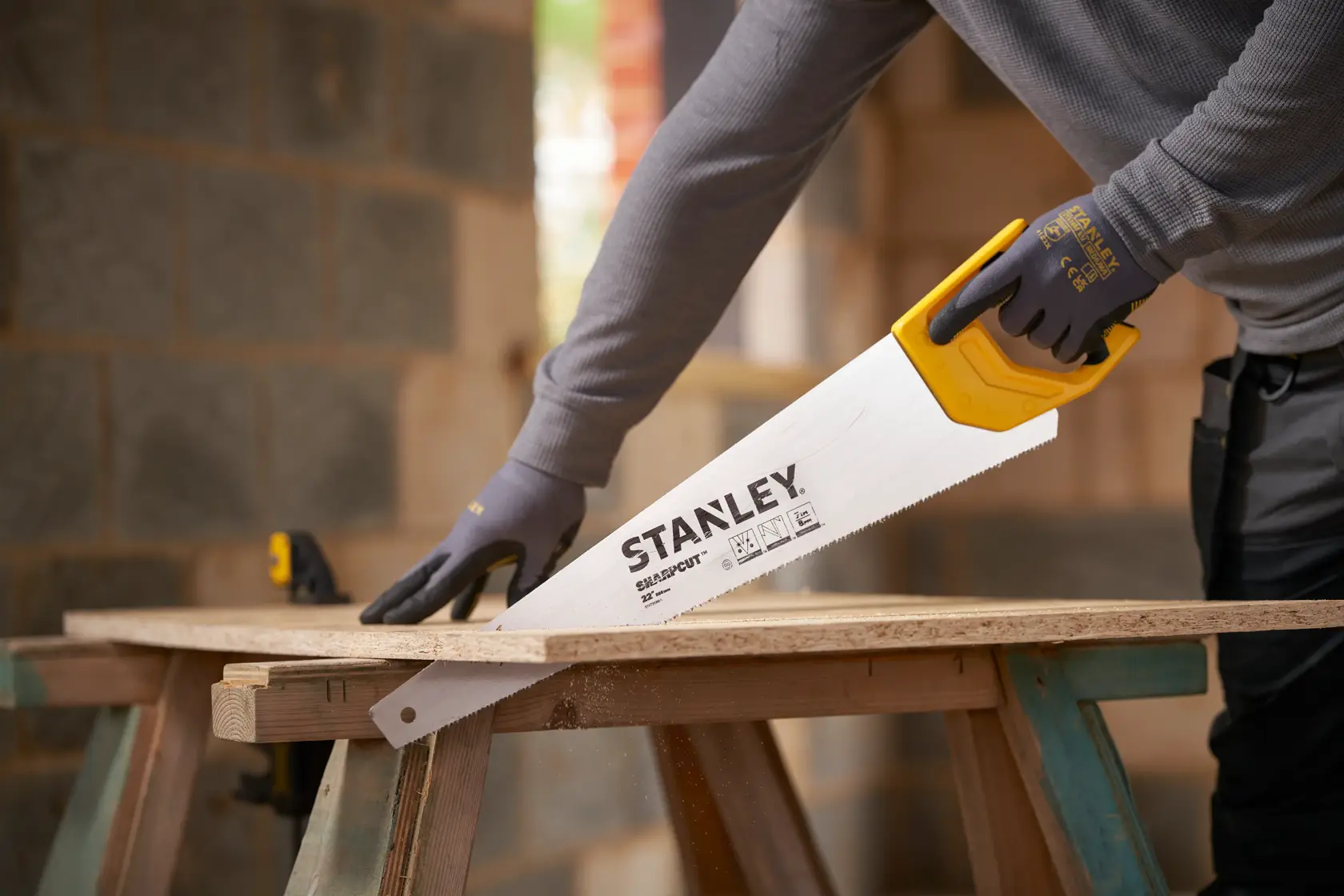 Foto der STANLEY STHT20368-1 Handsäge mit gelbem Griff beim Schneiden von Holz auf einer Baustelle.
