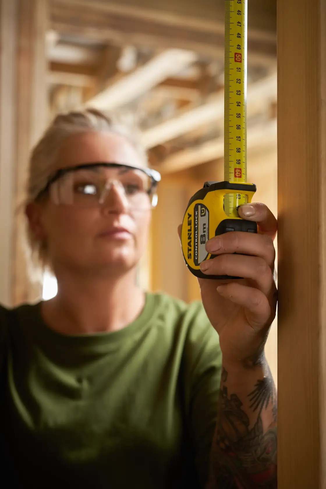 Foto vom STANLEY STHT37232-0 Maßband bei Benutzung an Holzrahmen durch Person mit Schutzbrille.