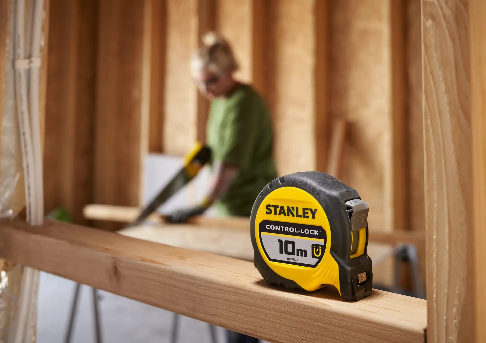 STANLEY STHT37233-0 10m Maßband auf Holzbalken, Baustelle im Hintergrund, Seitenansicht.