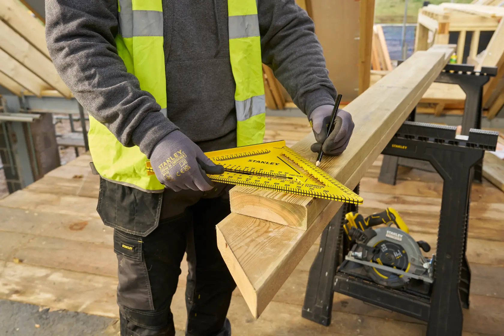 STANLEY STHT46013-0 gelbes Zimmermannswinkel zum Anzeichnen von Holz auf Baustelle, Arbeiter trägt Handschuhe.