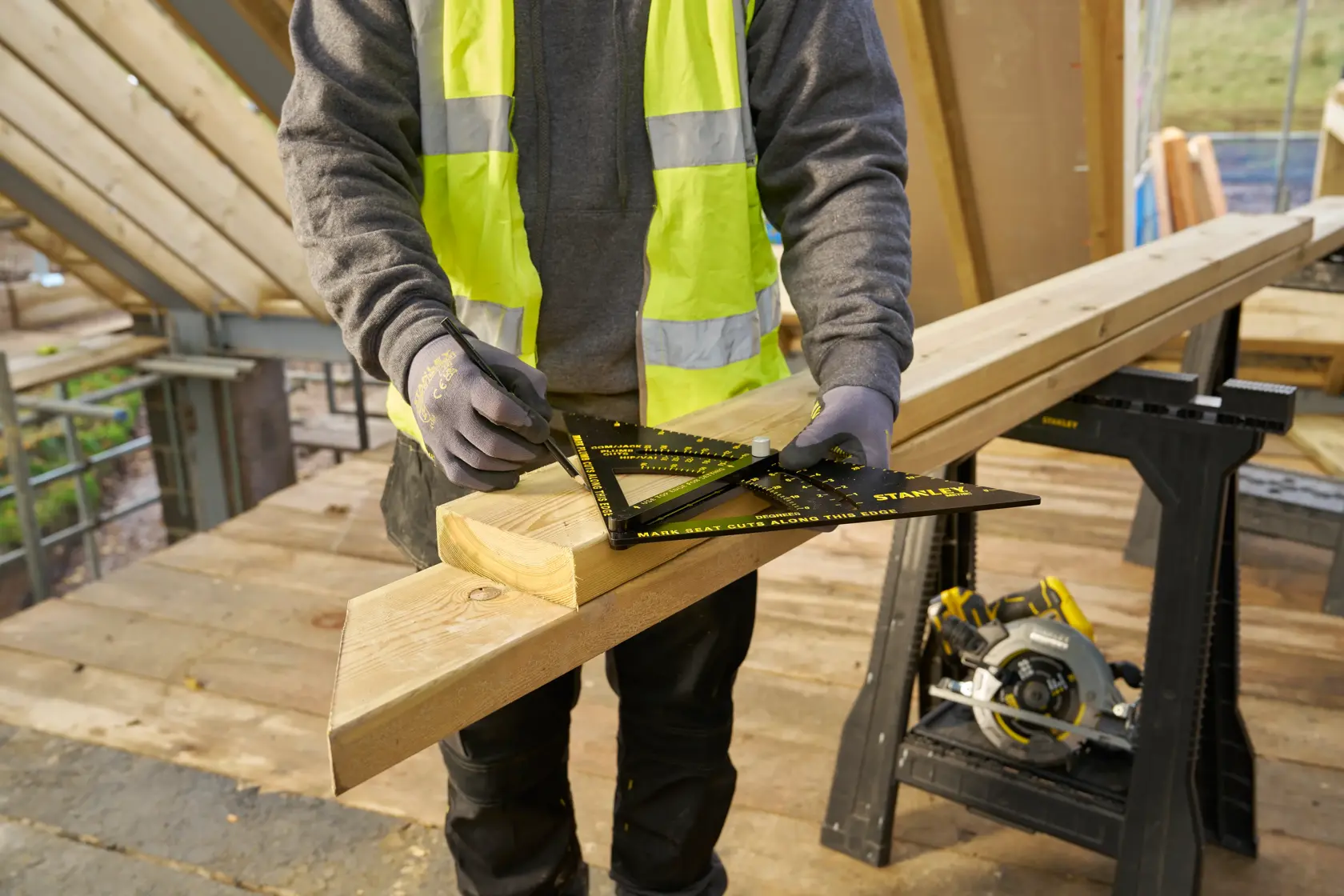 STANLEY STHT46054-0 Zimmerer markiert Holz mit schwarz-gelbem Winkel, Baustelle im Hintergrund.