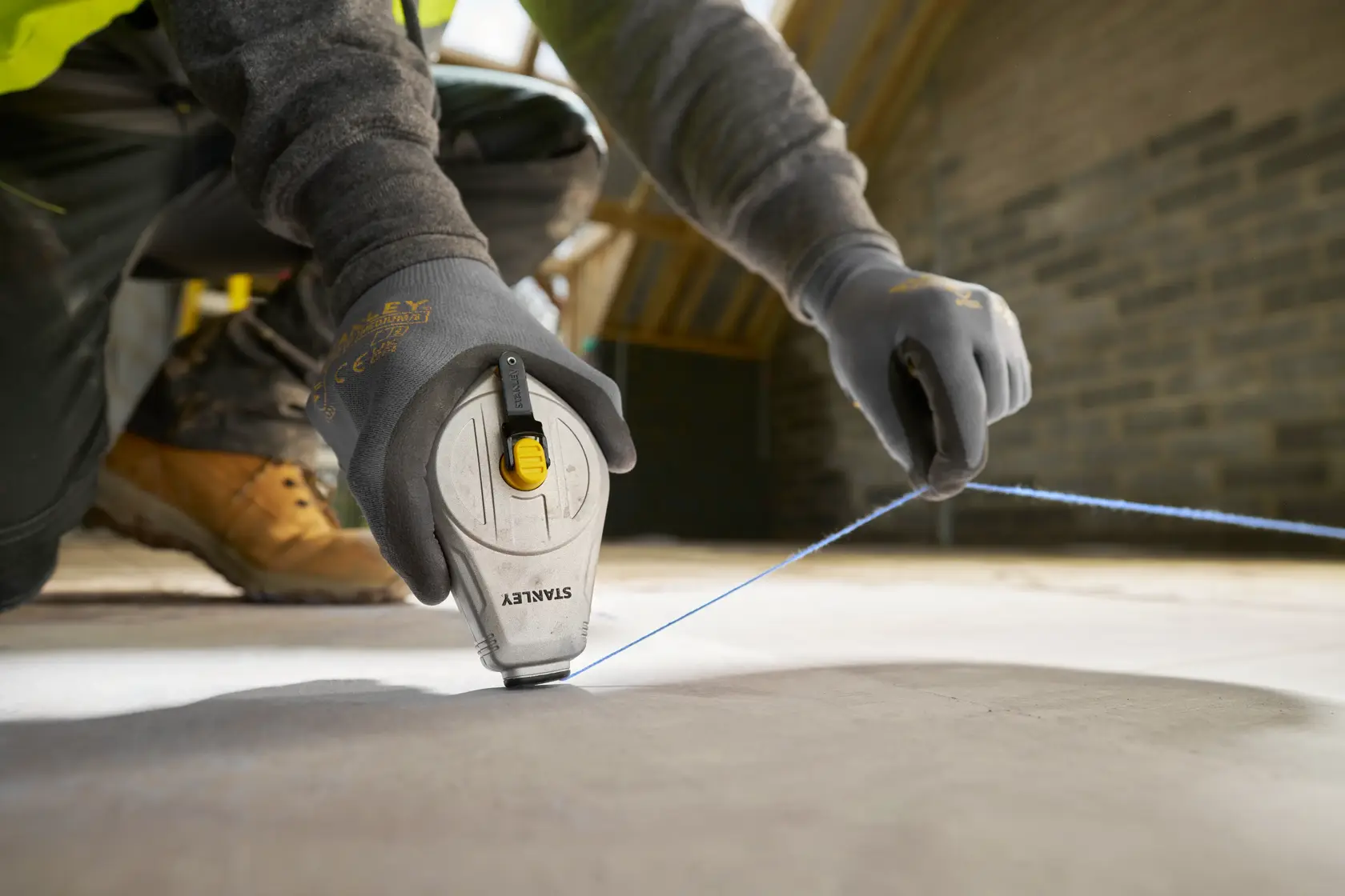 STANLEY STHT47110-0 Schlagschnur im Einsatz auf Baustelle, Nahaufnahme behandschuhter Hände mit blauer Schnur.