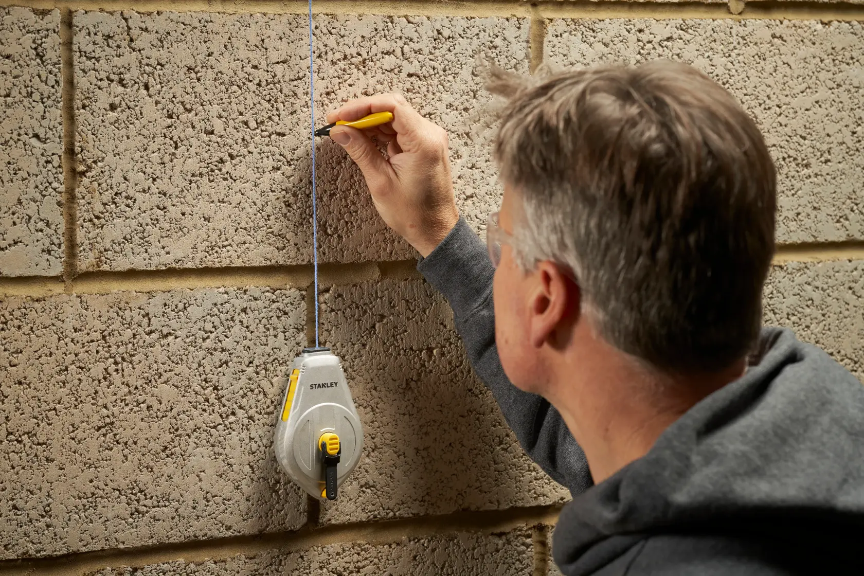 STANLEY STHT47110-0 Schlagschnur wird an einer Betonwand verwendet, Person markiert eine gerade Linie.