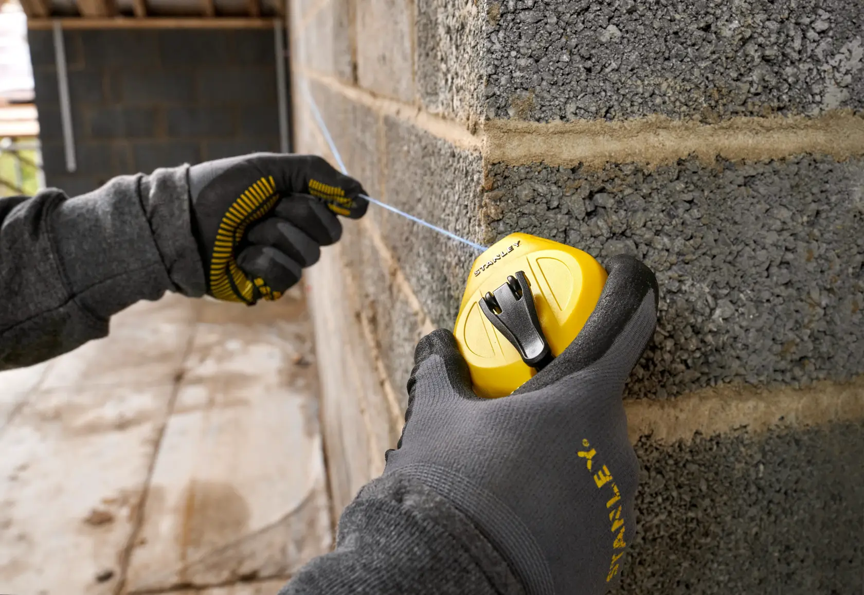 STANLEY STHT47112-0 Schlagschnurrolle im Einsatz an Betonwand, Nahaufnahme mit Handschuhen.