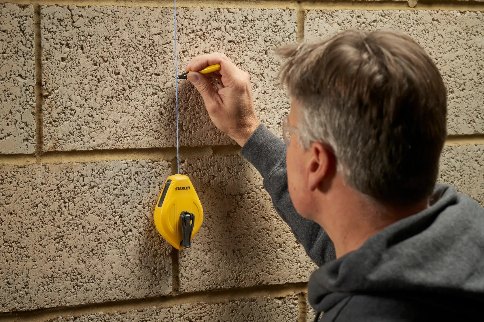 Foto von STANLEY STHT47112-0 Schlagschnur zum Markieren einer geraden Linie an einer Betonwand, Seitenansicht.
