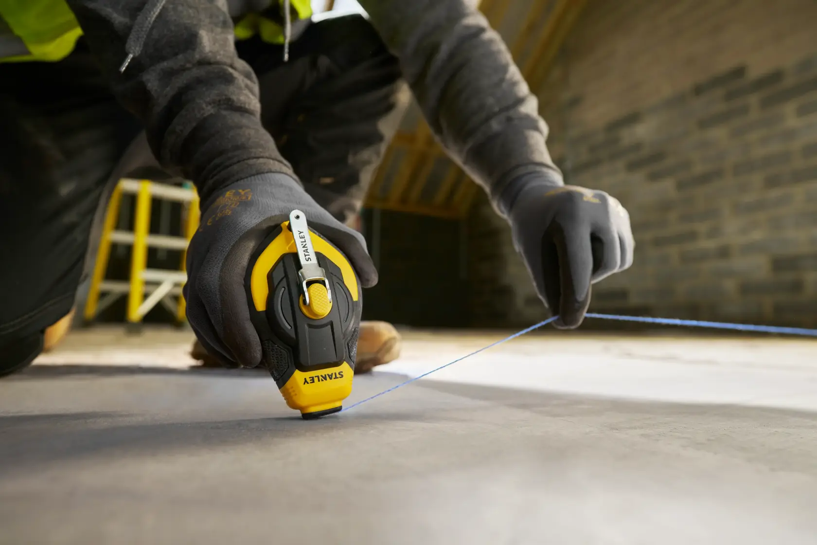 Foto des STANLEY STHT47311-0 Markierschnurwerkzeugs im Einsatz, Arbeiter markiert Linie auf Betonboden.