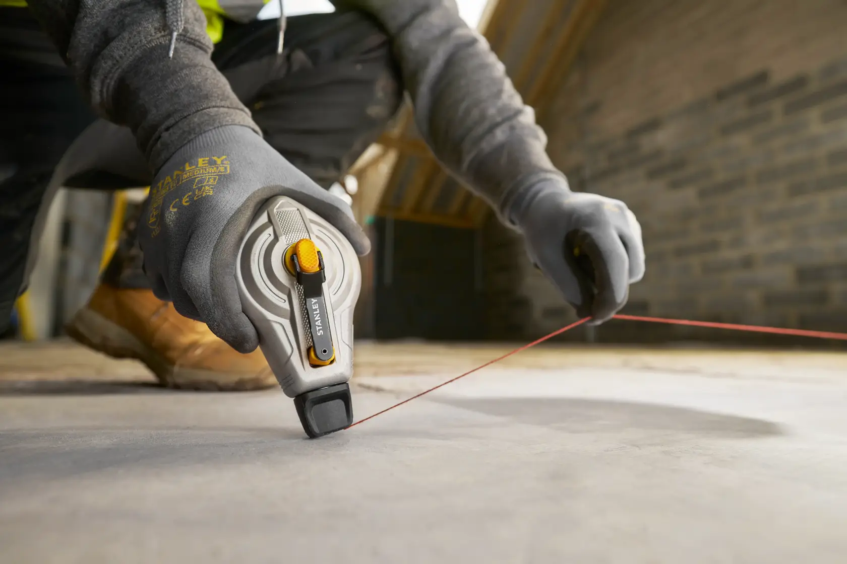 Foto der STANLEY STHT47611-0 Schlagschnurrolle im Einsatz auf Baustellenboden, Arbeiter mit Handschuhen.