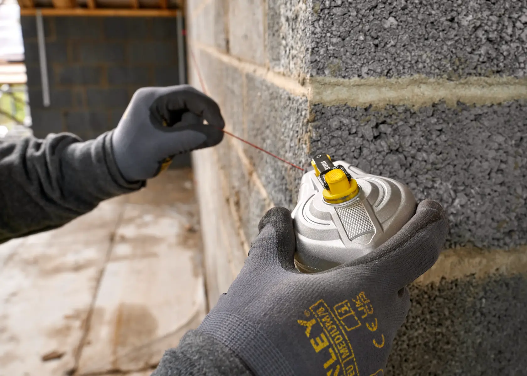 STANLEY STHT47611-0 Markierungsgerät von einer behandschuhten Hand an einer Mauer, Nahaufnahme Fotografie.