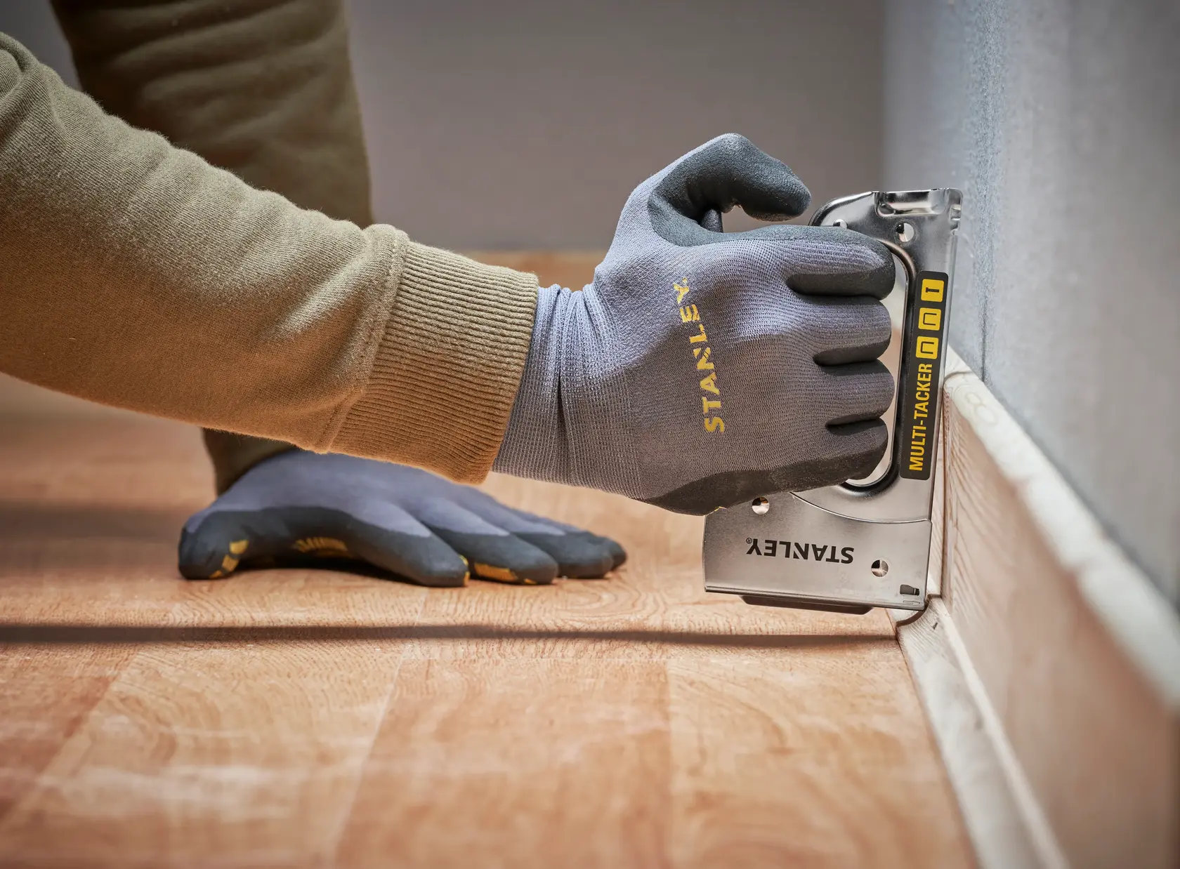STANLEY STHT6-70410 Multi-Tacker bei Bodenarbeit, Nahaufnahme einer behandschuhten Hand an der Wand.