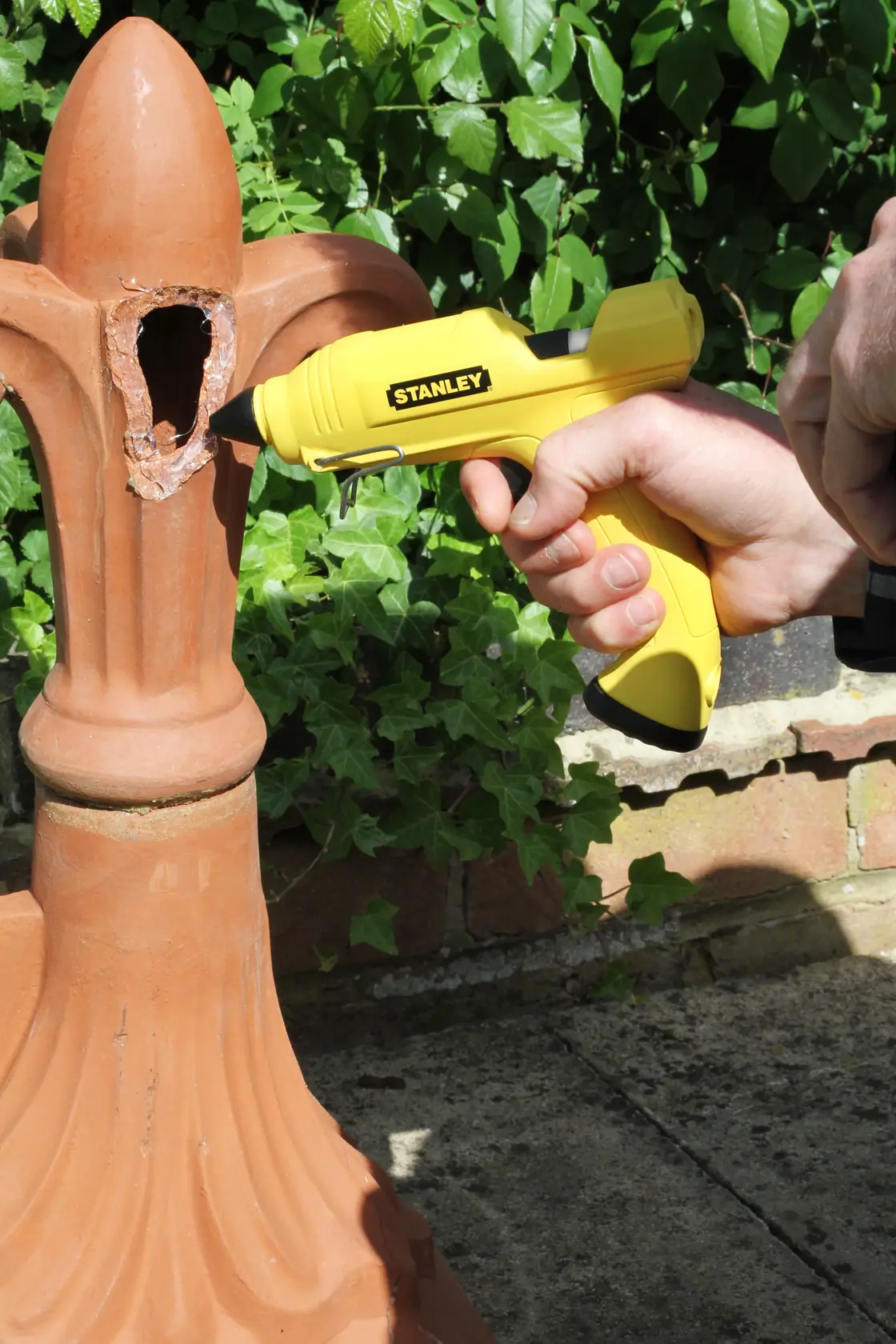 Stanley STHT6-70416 gelbe Heißklebepistole auf Außendekoration aus Keramik, Nahaufnahme, Gartenhintergrund.