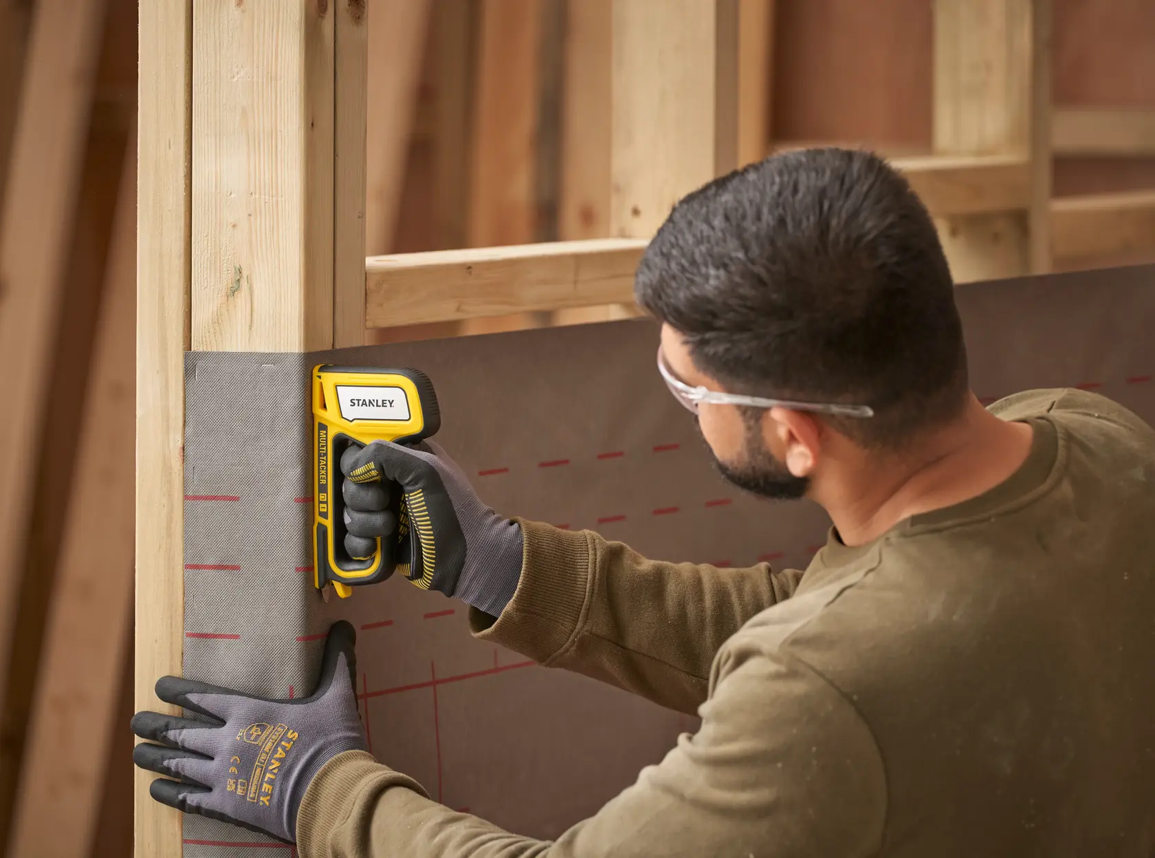 Stanley STHT70440-0 Tacker befestigt Blatt am Holzrahmen, Nutzer trägt Handschuhe und Schutzbrille.