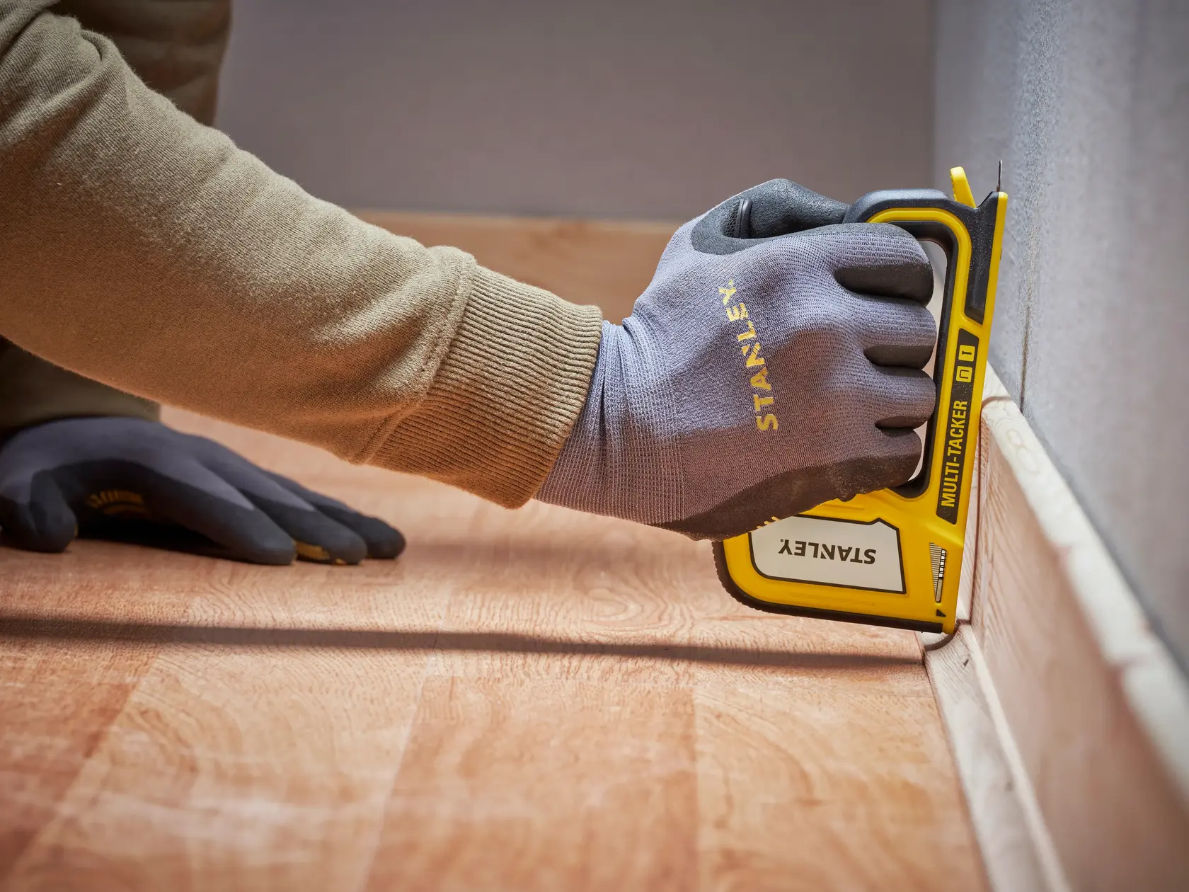Foto vom STANLEY STHT70440-0 Tacker im Einsatz, behandschuhte Hand befestigt Sockelleiste, Seitenansicht.