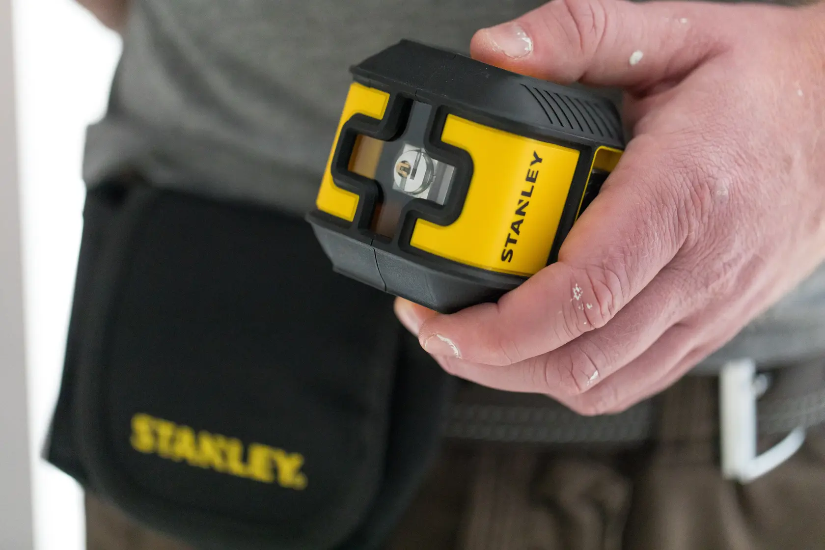 Foto vom STANLEY STHT77499-1 Laser-Nivelliergerät in der Hand, gelb-schwarz mit STANLEY Werkzeugtasche.