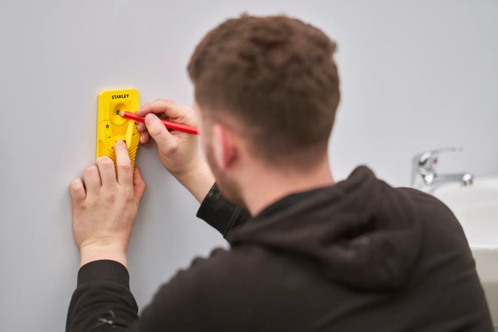 STANLEY STHT77587-0 gelber digitaler Balkenfinder im Einsatz an Wand neben Waschbecken, Fotografie.