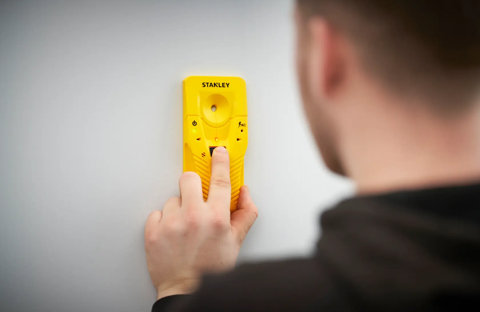 Foto vom gelben STANLEY STHT77587-0 Balkensucher an weißer Wand, gehalten von einer Person.