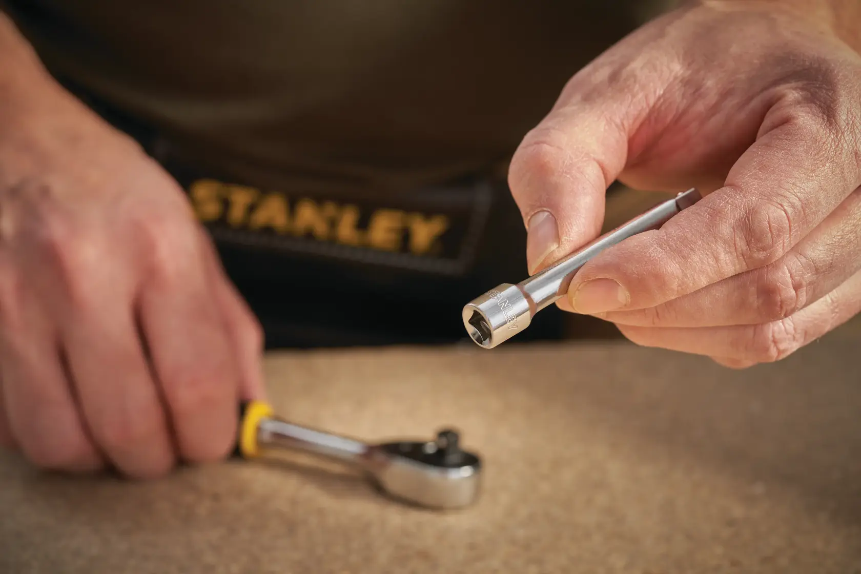 STANLEY STMT86006-0 Stecknuss-Verlängerung in der Hand gehalten, Ratsche im Hintergrund, Nahaufnahme.
