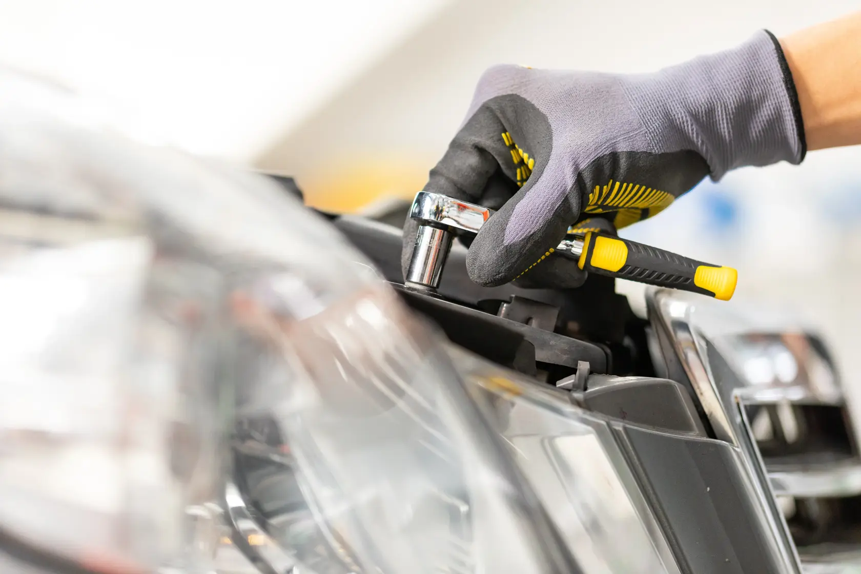 STANLEY STMT86111-0 Ratsche wird von einer behandschuhten Hand an einem Autoscheinwerfer verwendet, Nahaufnahme.