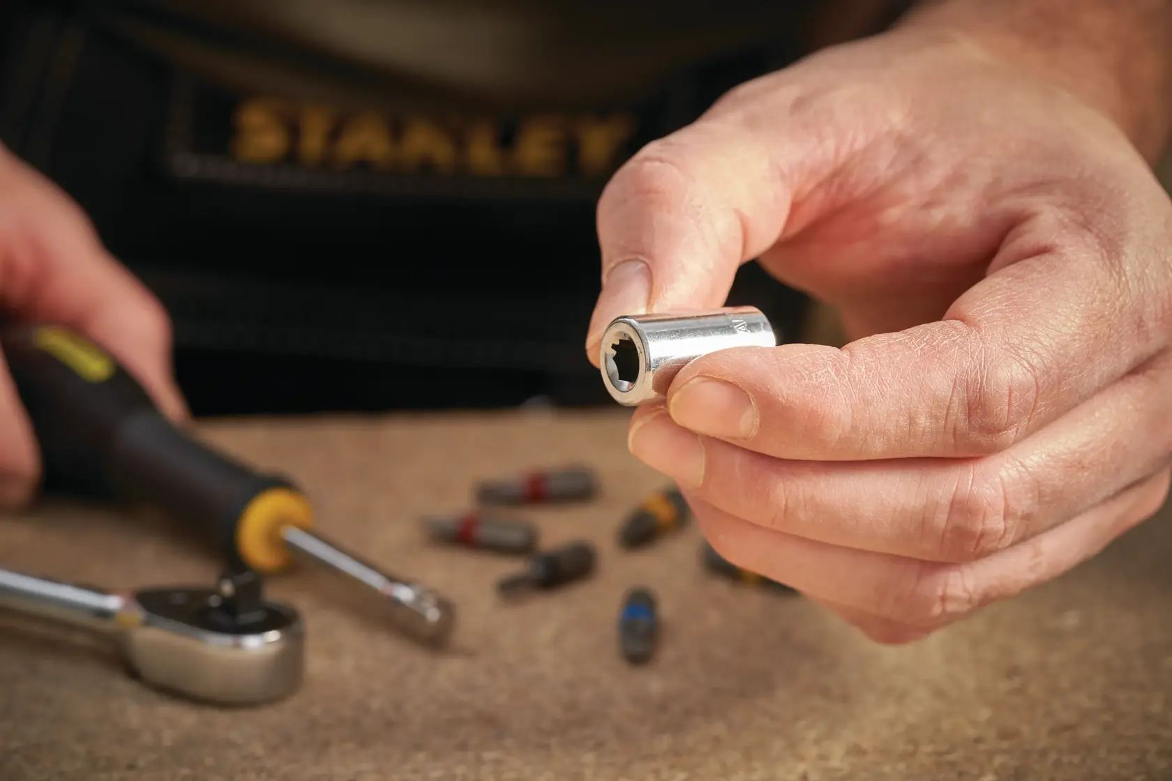 STANLEY STMT86124-0 Steckschlüssel-Bit in der Hand, Ratsche und Bits auf Werkbank, Nahaufnahme.
