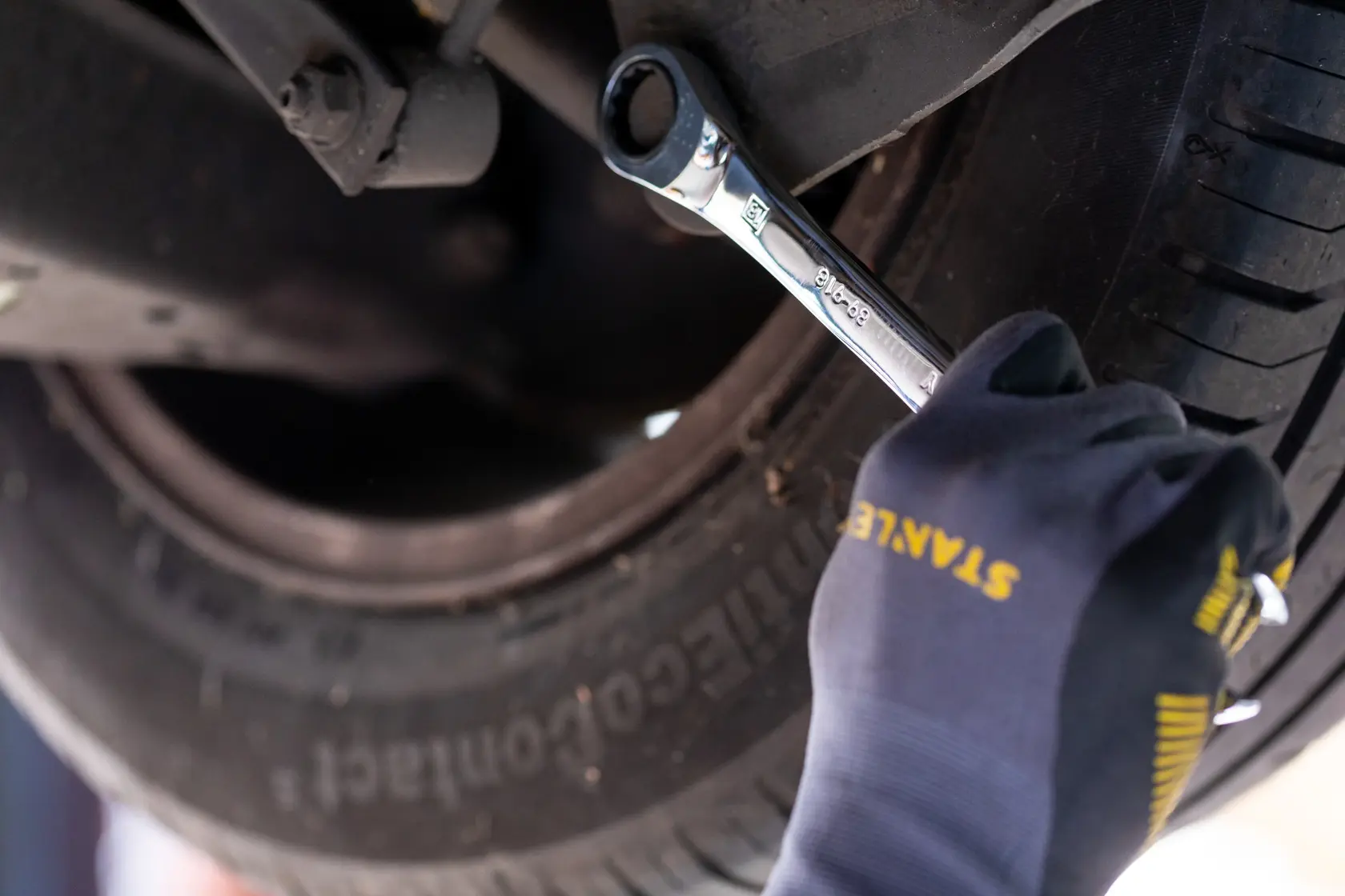STANLEY STMT89915-0 Ratschen-Schlüssel am Autoreifen, Nahaufnahme mit behandschuhter Hand.