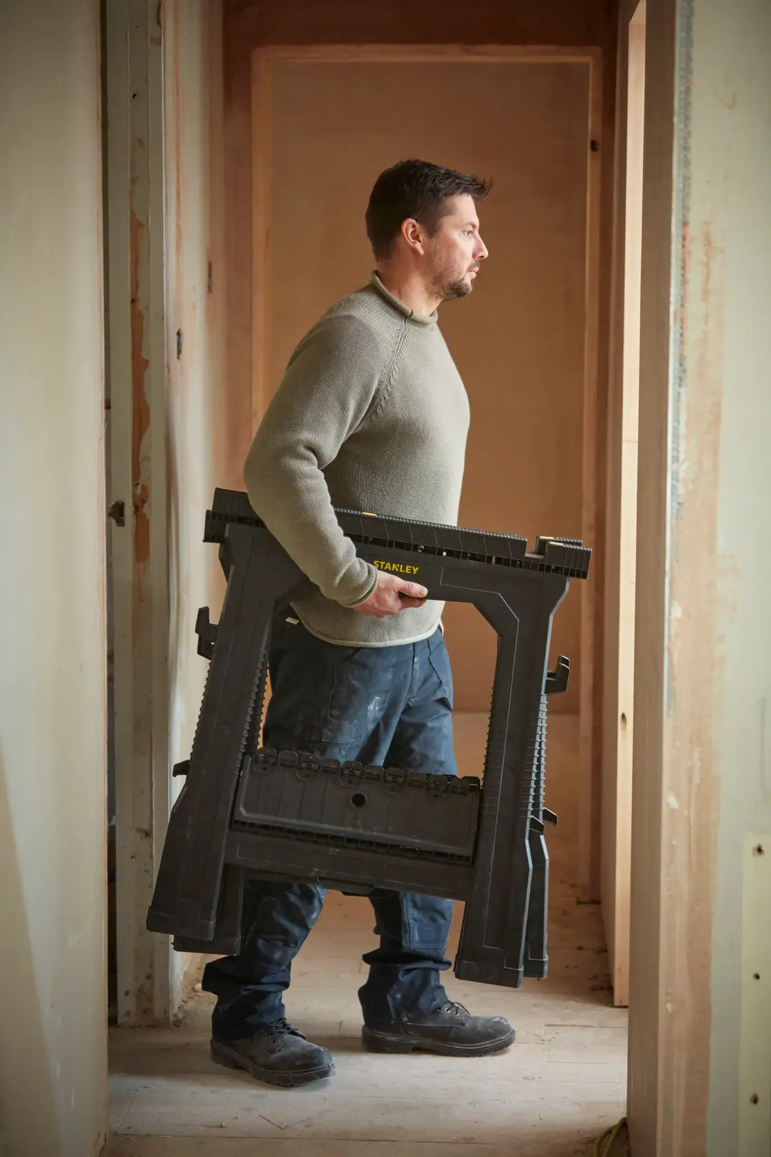 Foto einer Person mit zusammengeklapptem STANLEY STST1-70713 Sägebock auf einer Baustelle.