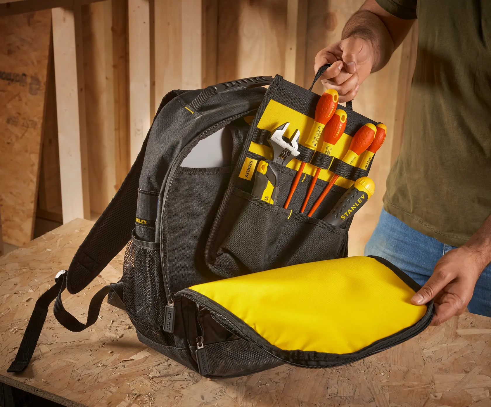 STANLEY STST1-72335 Werkzeugrucksack offen mit sortierten Werkzeugen in den Innenfächern auf Holzfläche.
