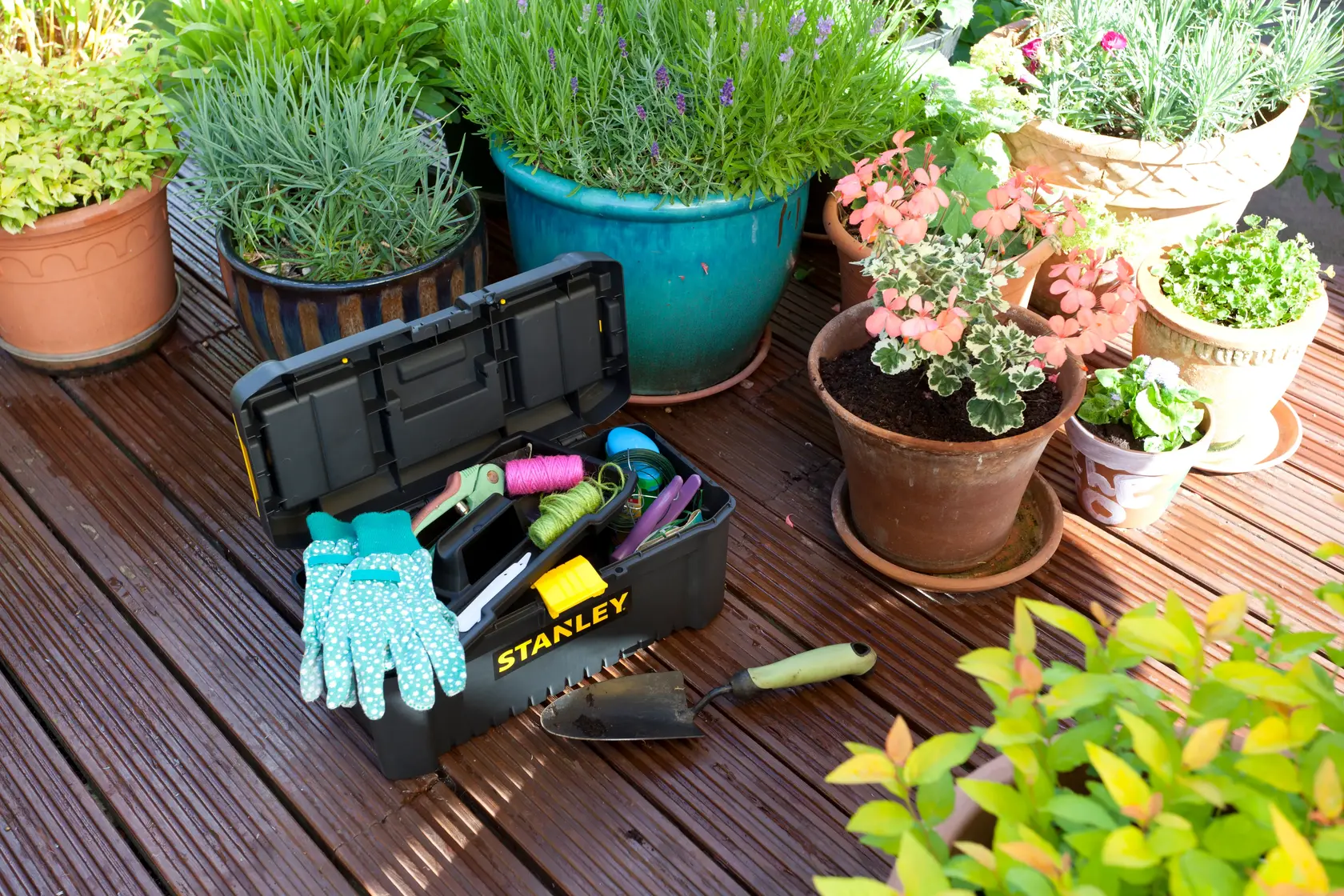 STANLEY STST1-75517 Werkzeugkasten mit Gartenhandschuhen und Werkzeug auf Holzdeck bei Topfpflanzen, schräg.