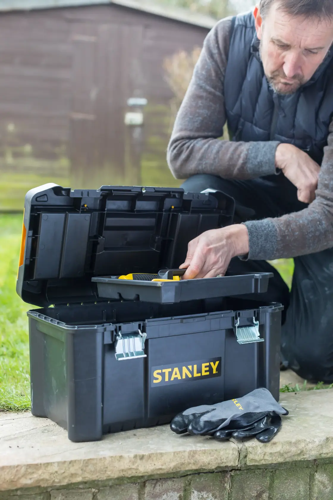 STANLEY Werkzeugkiste STST1-75521, STST1-75521-KR außen, Deckel offen, Handschuhe, Mann greift nach Einsatz.