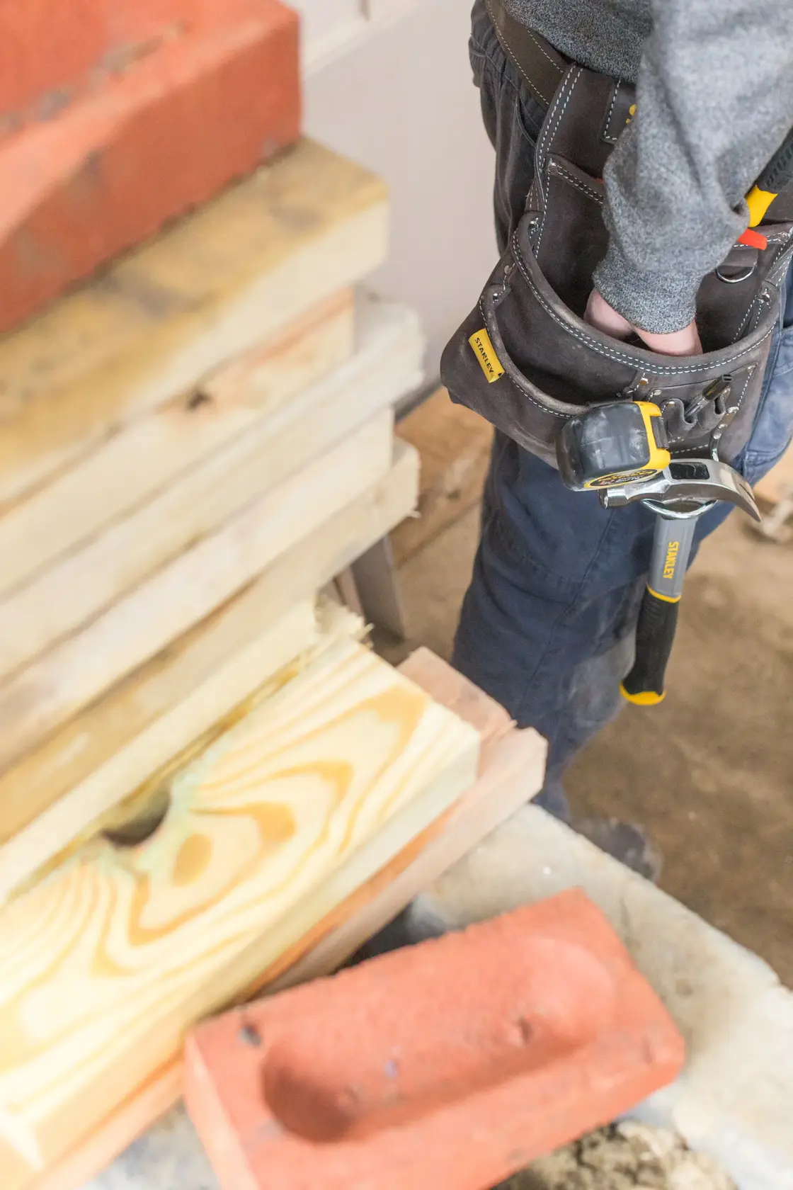 STANLEY STST1-80114 Werkzeuggürtel mit Hammer, getragen neben Holz und Ziegel, Seitenansicht Foto.
