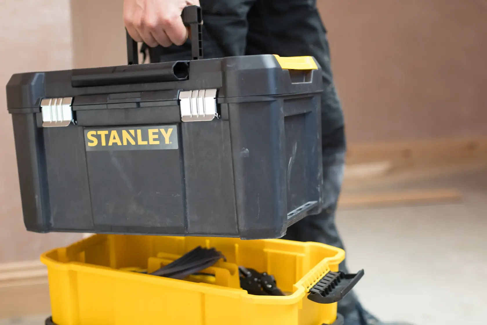 Foto von STANLEY STST1-80151 Werkzeugkasten, getragen über einem offenen gelben Behälter, Innenbereich.