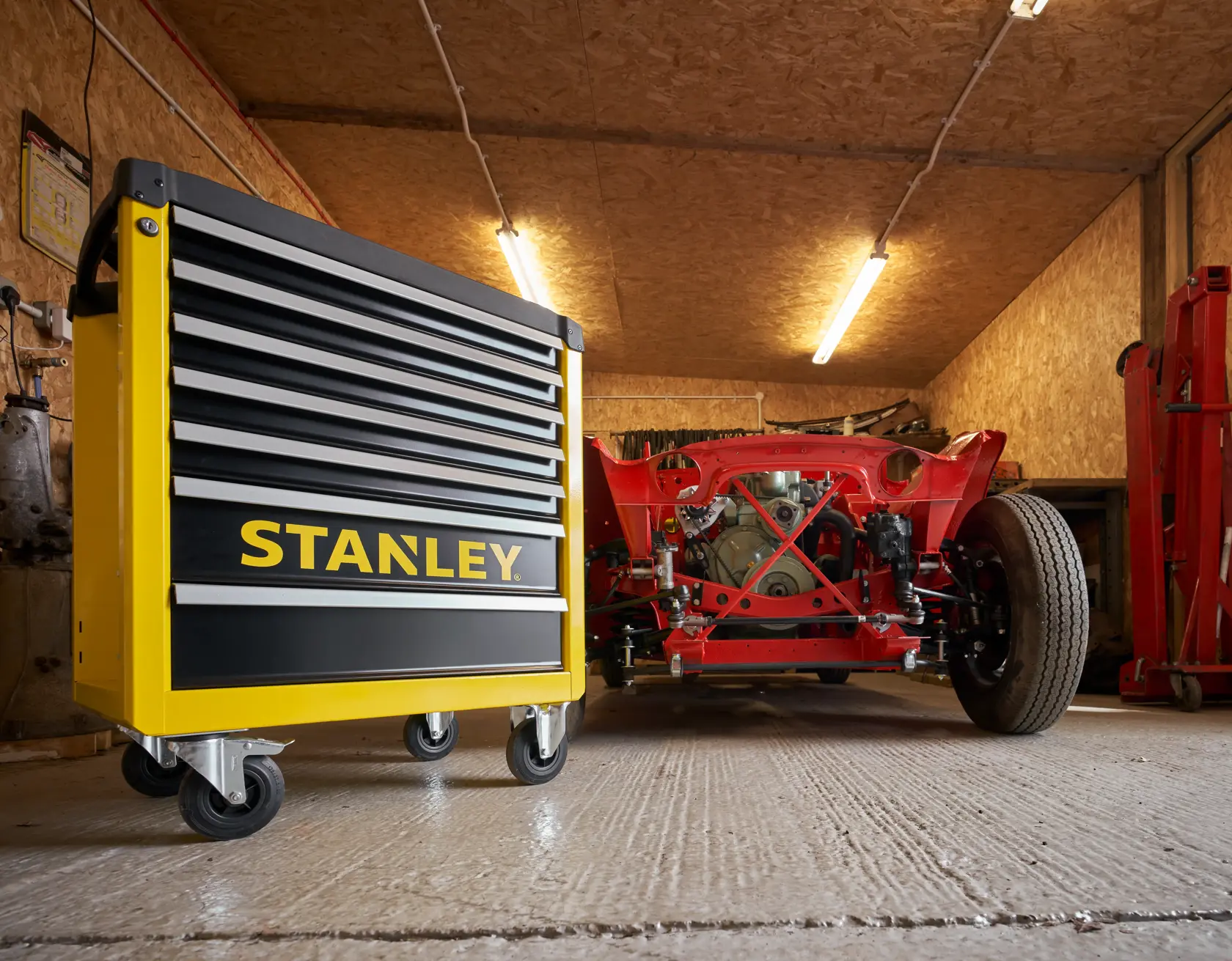 STANLEY STST74306-1 gelb-schwarzer Rollwerkzeugkasten in Garage, niedriger Winkel, neben rotem Fahrgestell.