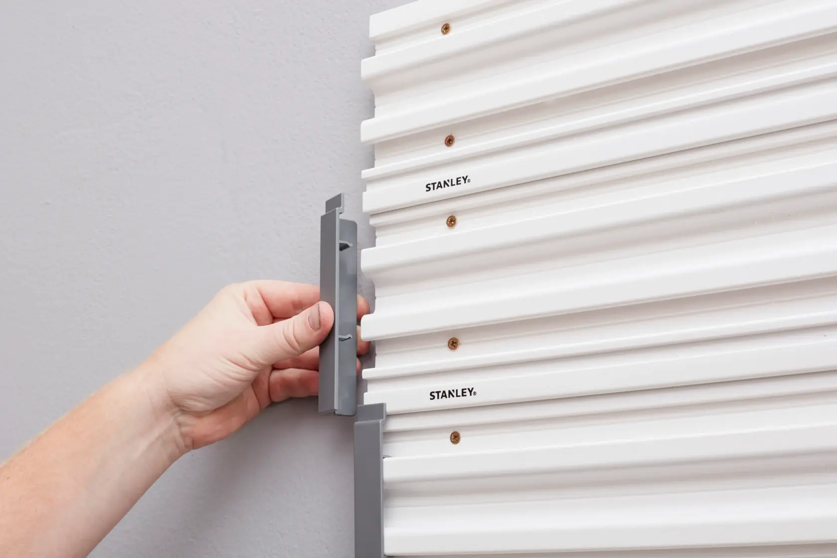 STANLEY STST82611-1 Hand installiert grauen Haken an weißer Wandtafel, Nahaufnahme seitlich.