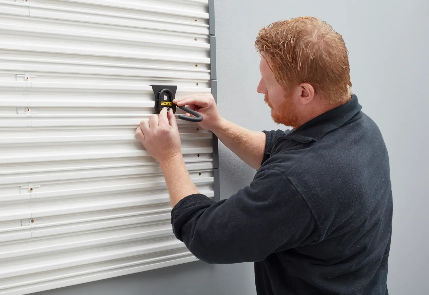 Stanley STST82616-1 Wandhaken wird von einer Person an einer weißen, gewellten Wand montiert.