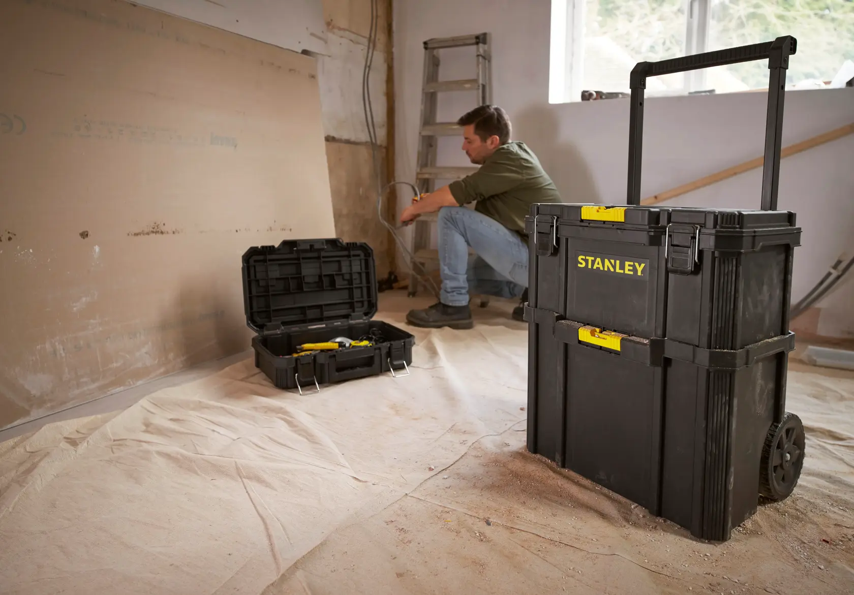 STANLEY STST83319-1 schwarze Rollwerkzeugkiste mit gelben Verschlüssen auf Baustelle, Mann benutzt passende Toolbox.