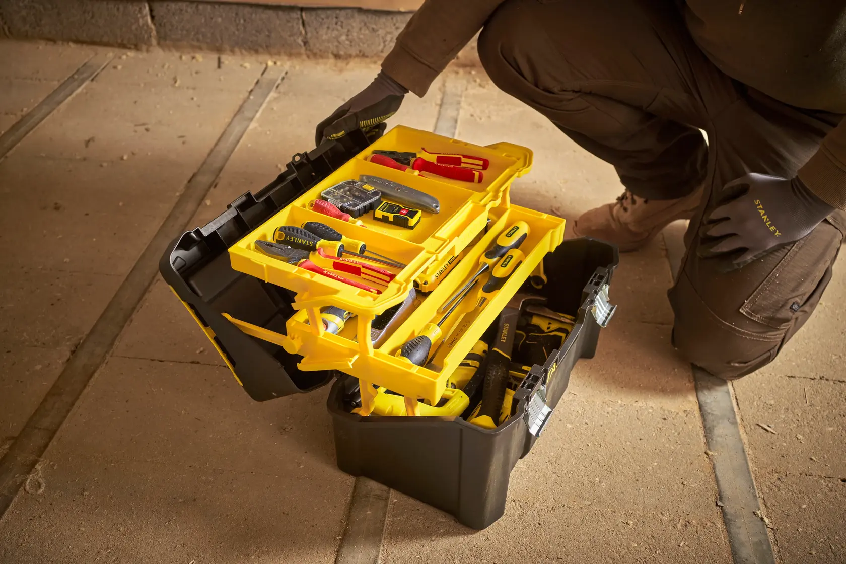 STANLEY STST83397-1 schwarze und gelbe Werkzeugbox mit Fächern und Werkzeugen, geöffnet auf Werkstattboden.